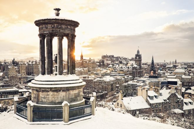 The historic city centre of Edinburgh covered in snow, taken at sunset from Calton Hill in December, with the historic Dugald Stewart Monument in the foreground.