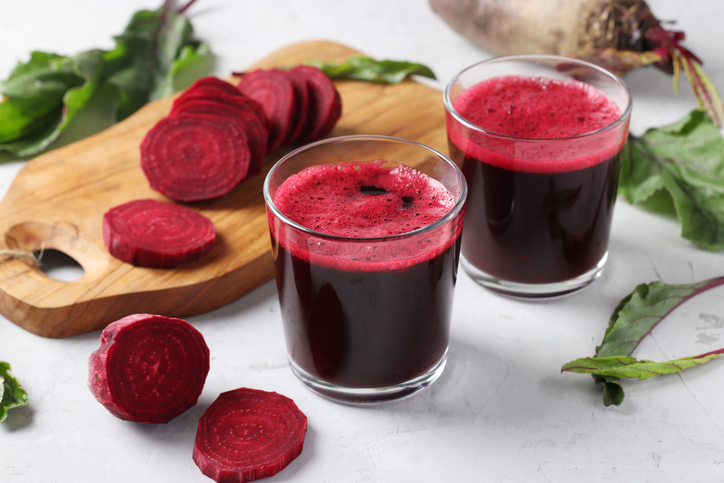 Two glass of fresh beetroot juice and chopped beet on wooden board on gray background.