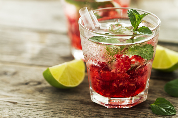 Tasty cold fresh drink lemonade with raspberry, mint, ice and lime in glass on wooden background. Closeup.