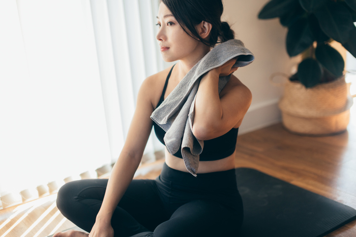 Cropped shot of a young Asian woman feeling exhausted, wiping sweat with a towel, after doing yoga.