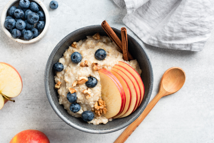 Oatmeal porridge with apple, cinnamon and blueberries in bowl on grey concrete background, top view. Healthy breakfast food for autumn. Comfort food